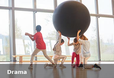 In a drama hall, three children hold a giant globe above their heads, another child is dancing
