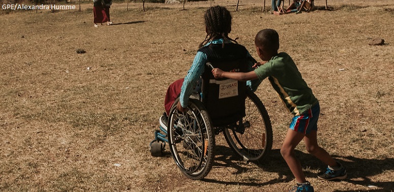 A student pushes his classmate in a wheelchair in the school yard
