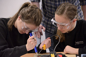 Two secondary school girls with protective glasses are soldering