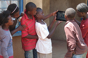 School children stand looking at something on a tablet computer