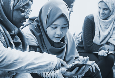 Young women sit talking, looking at something on a smart phone