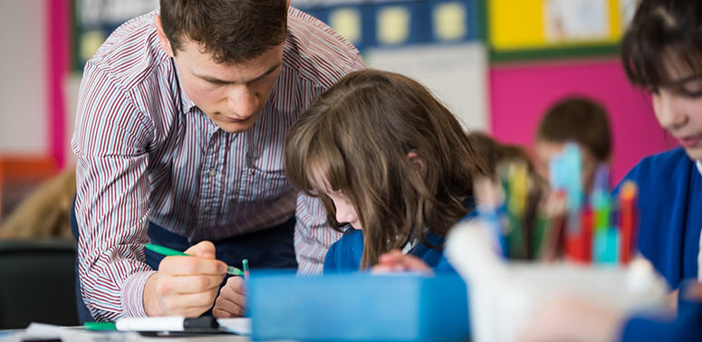 A primary teacher supports a pupil with writing