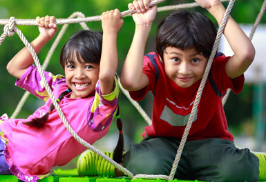 two children smiling and playing on a rope bridge