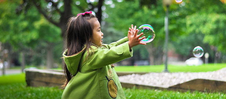 Young girl outside popping bubbles between her hands 