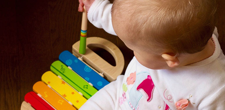 A baby sits and playing a wooden instrument