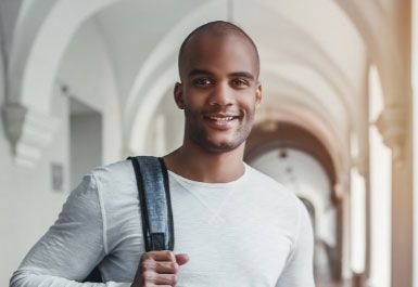 A student in a long arched passageway smiles at the camera