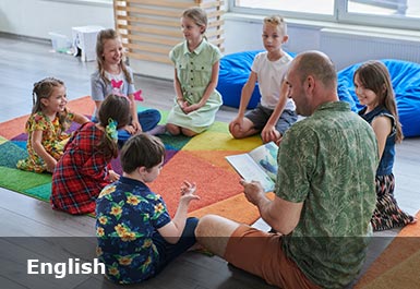 A smiling teacher and children sit on the floor reading 