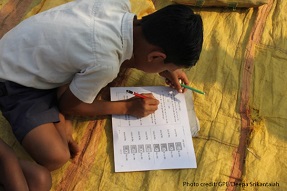 Boy sits doing homework on carpet, India