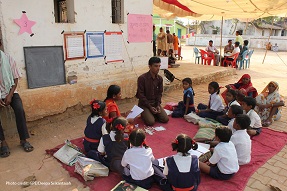 Male teachers gives a class to students outside on a carpet, India