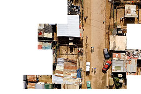 An aerial view of a shanty town with people and cars moving along a dirt road
