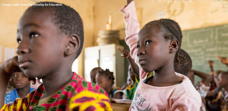 A young African girl in class with hand in the air