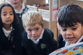 A primary school pupil reads an open book to other children