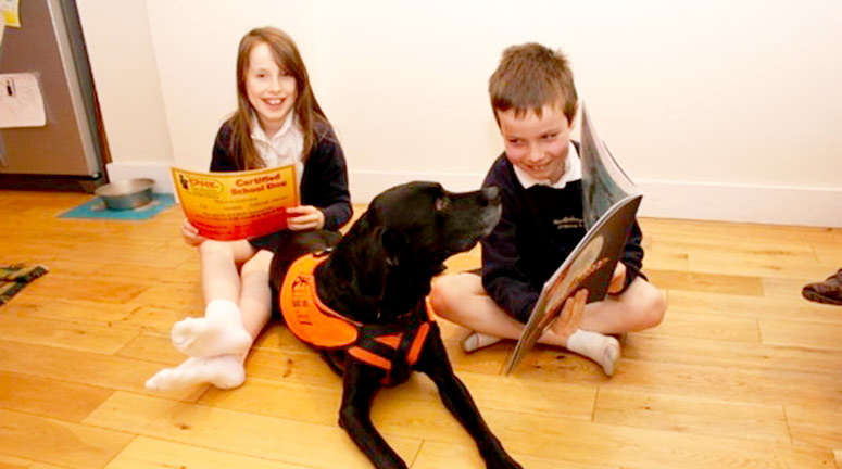 two children smiling and reading to a dog