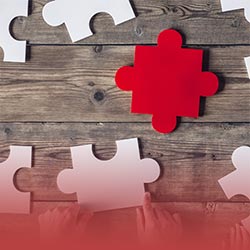 People around a table hold large white jigsaw pieces surrounding a single red jigsaw piece