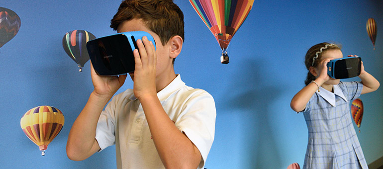 An image of hot air baloons on a classroom wall while children watch on VR headsets
